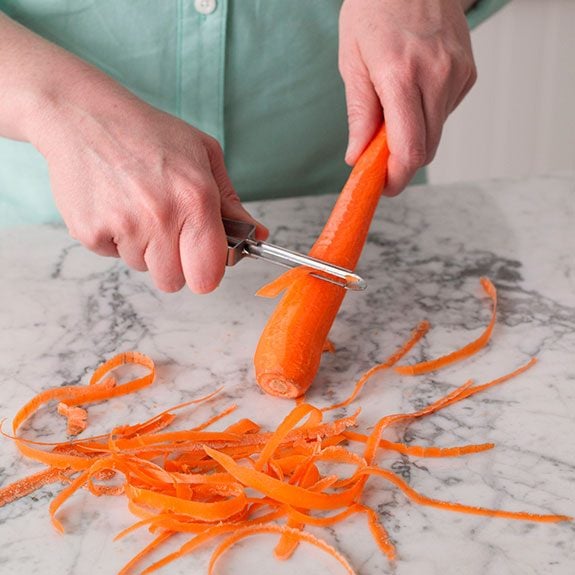 person holding a carrot and peeling from the center to the end