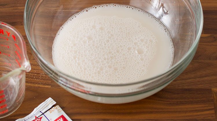 Sourdough starter sits in a large glass bowl beside an open yeast packet