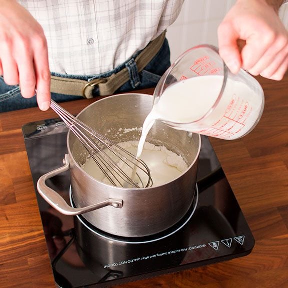 A person using a measuring cup to pour in milk to the mixture as they whisk