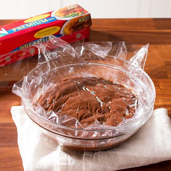 Pudding covered in plastic wrap in a glass bowl and left to cool
