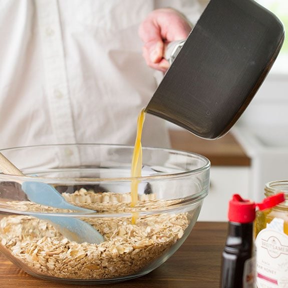 person pouring liquid from a saucepan into the dry granola ingredients