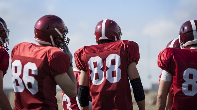 Football players standing side-by-side with their backs to the camera displaying their red jerseys and numbers