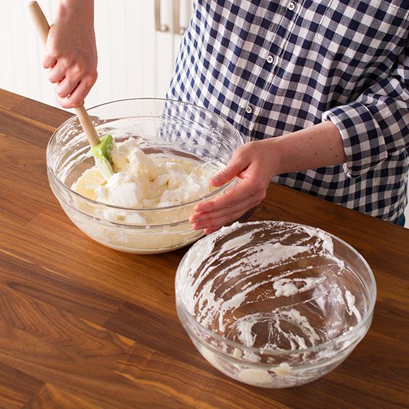 Person using a green spatula to fold in the egg whites to the mixture